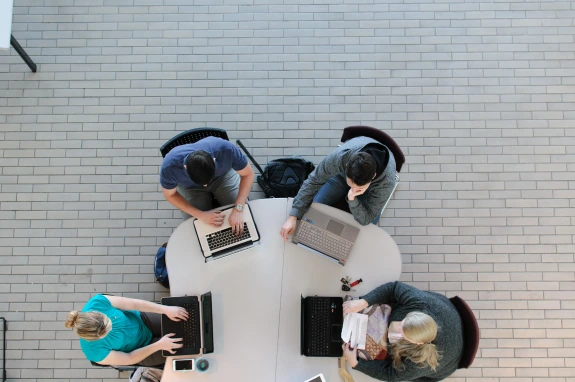 Four students sitting at a table using laptops.