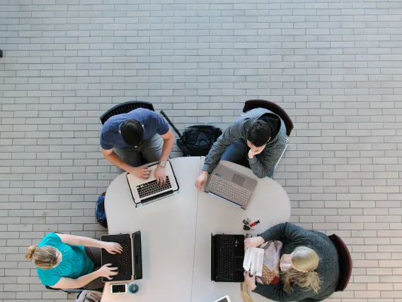 Four students sitting at a table using laptops.